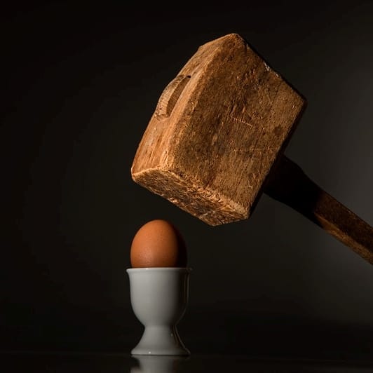 a wooden mallet held over an egg to resemble threatening behaviour